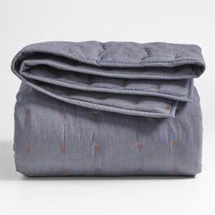 the grey blanket is folded up on top of it's pillow case, with an orange dot pattern