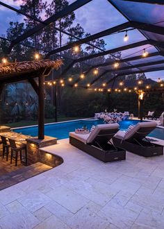 an outdoor dining area next to a swimming pool at dusk with string lights hanging from the ceiling