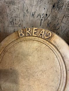 the word bread is carved into an old wooden bowl with writing on it and in front of graffiti covered walls