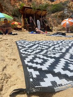 a black and white blanket sitting on top of a sandy beach