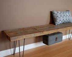 a wooden bench with hairpin legs and a pillow on it next to a wall