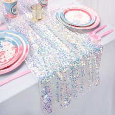 the table is set with pink and blue plates, silver sequins, and napkins