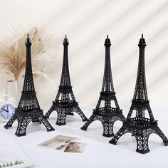 three miniature black metal eiffel tower models on a white table next to a clock