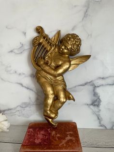 a golden angel figurine sitting on top of a red box next to a white flower