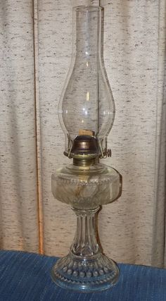 an old fashioned oil lamp sitting on top of a blue tablecloth covered floor next to a curtain