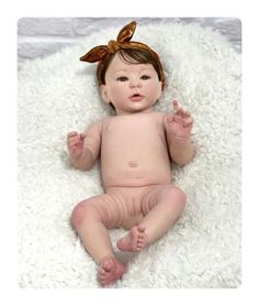 a baby doll with a bow on her head laying on a fluffy white blanket and looking at the camera