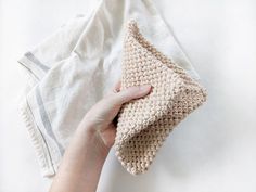 a hand holding a crocheted purse on top of a white cloth next to a towel