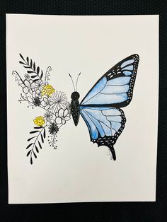 a blue butterfly sitting on top of a white paper with yellow and black flowers around it