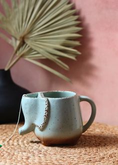 a coffee cup sitting on top of a table next to a plant