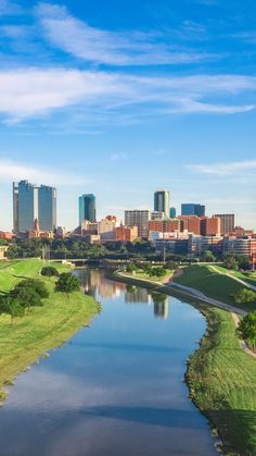 a river running through a lush green park next to tall buildings and a city skyline