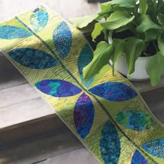 a blue and yellow quilted table runner next to a potted plant on a porch