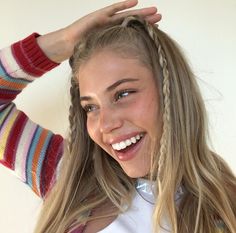 a woman with long blonde hair is smiling and holding her hands up to her head