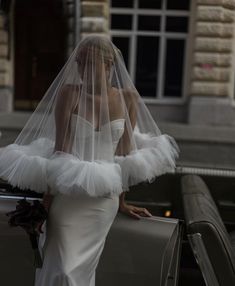 a woman in a wedding dress and veil standing next to a car