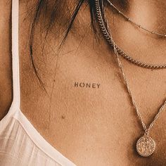 the back of a woman's neck with two necklaces and a coin on it