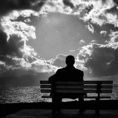 a man sitting on top of a bench next to the ocean under a cloudy sky