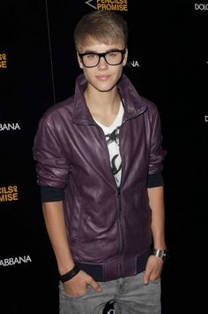 a young man wearing glasses and a leather jacket standing in front of a black background