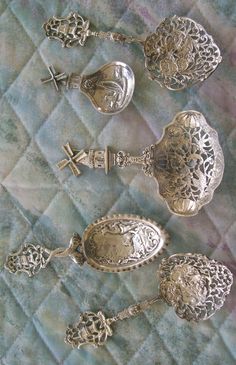 three silver spoons sitting on top of a blue quilted tablecloth with crosses