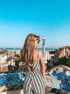 a woman standing on top of a building next to a blue tiled roof with the city in the background