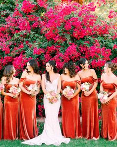 a group of women in long dresses standing next to each other with flowers behind them