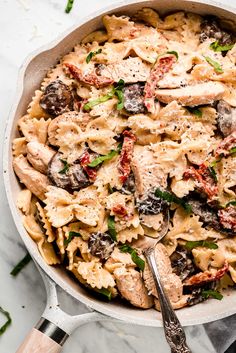 a skillet filled with pasta and meat on top of a marble countertop next to a spatula