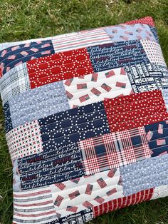 a red, white and blue patchwork pillow sitting on the grass with it's cover