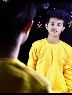 a young man standing in front of a mirror talking to another person who is wearing a yellow shirt