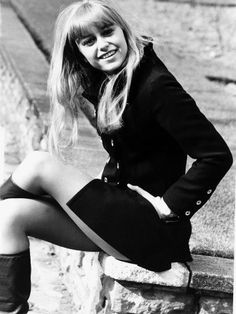 a woman sitting on top of a stone wall next to a brick wall with her legs crossed