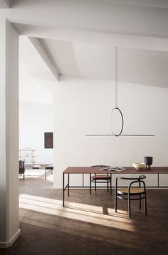 a dining room table and chairs in front of a white wall with an oval light fixture hanging from the ceiling