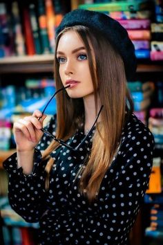 a woman with long hair wearing glasses and a black hat is standing in front of bookshelves