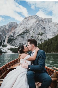 a bride and groom kissing on the bow of a boat in front of a mountain lake