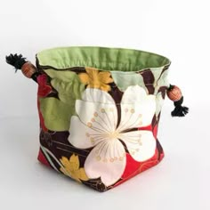 a flowered fabric basket with tassels and pompoms on the handles