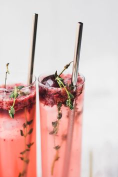 two glasses filled with pink liquid and garnished with green sprigs on the rim