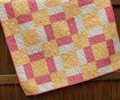 a pink and yellow quilt hanging on the side of a wooden fence