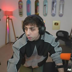 a young man wearing headphones sitting in front of a computer desk with several skateboards on the wall behind him