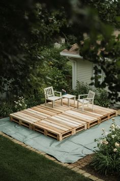 two chairs sitting on top of a wooden platform in the middle of a garden area