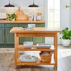 a kitchen with green cabinets and white dishes on a wooden table in front of a window