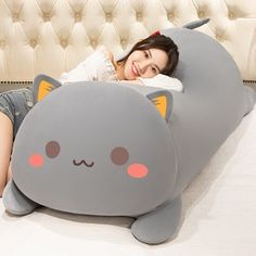 a woman laying on top of a bed with a gray pillow shaped like a cat