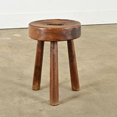 a small wooden stool sitting on top of a cement floor next to a white wall