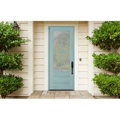 a blue front door on a white house with potted plants and bushes around it