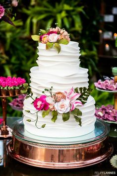 a white wedding cake with pink flowers and greenery on the top is surrounded by other desserts