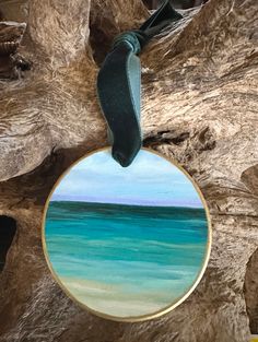 a blue and green painting hanging from a wooden tree branch with a ribbon around it