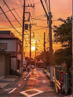 the sun is setting on an empty street with power lines in the foreground and people walking down the road