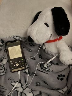 a stuffed dog laying on top of a bed next to a cell phone and headphones