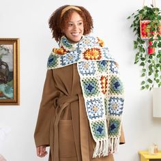 a woman wearing a crocheted shawl and scarf in front of a painting