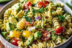 a bowl full of pasta salad with tomatoes, avocado and cilantro