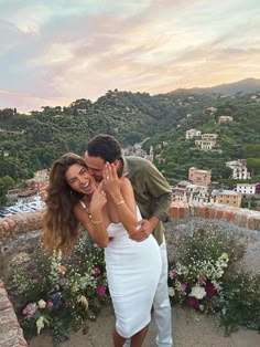 a man and woman embracing each other on top of a hill with flowers in the foreground