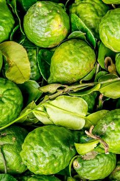 green fruit is piled up on top of each other with leaves in the foreground