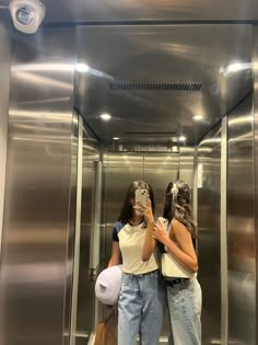 two women standing in front of an elevator taking a selfie with their cell phone