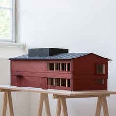 a red model house sitting on top of a wooden table in front of a window