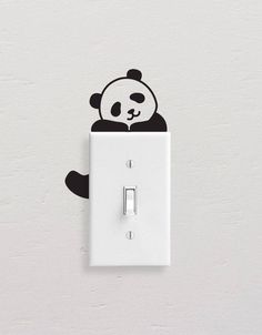 a black and white panda bear sitting on top of a light switch cover with its head sticking out